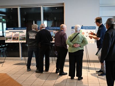Community members viewing project display boards at an evening open house. Description: Residents review project visuals and discuss shoreline resilience priorities during an open house.