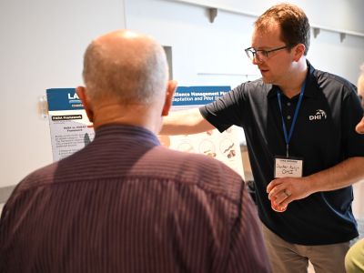 Project representative presenting information to attendees at a display board. Description: A project team member explains shoreline planning concepts and answers questions from community members.