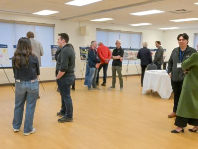 Wide view of attendees networking and viewing displays at an open house. Description: Community members and project staff gather to discuss shoreline priorities and future resilience planning initiatives.
