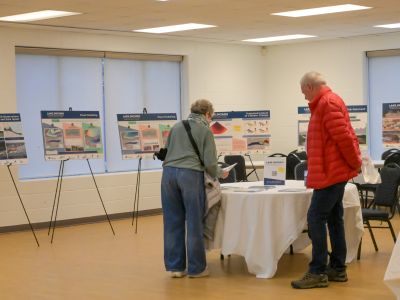 Two attendees reviewing display boards at a community open house. Description: Community members read project information boards and materials during a shoreline resilience engagement session.