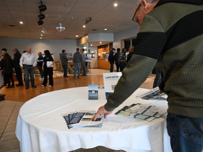 Alt text: Community members speaking with project staff at an open house display table. Description: Attendees gather around a registration and information table during a open house.