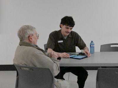 Project team member speaking with a community member at a table and filling out a survey on an iPad.